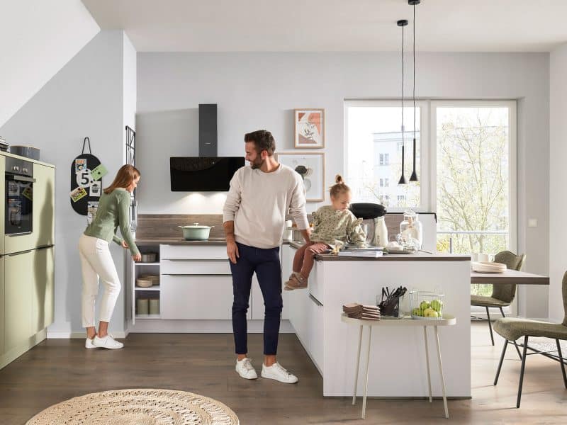 Eine dreiköpfige Familie verbringt ihre Zeit gemeinsam in einer modernen, hellen Küche mit grünem und weißem Dekor.